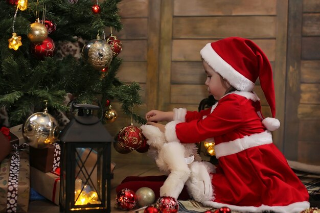 Piccolo bambino seduto davanti a un albero di Natale e gioca con i giocattoli