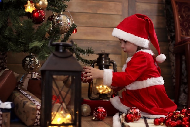 Piccolo bambino seduto per terra nella stanza davanti a un albero di Natale decorato