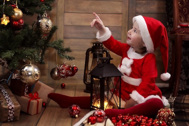 Piccolo bambino seduto per terra nella stanza davanti a un albero di Natale decorato