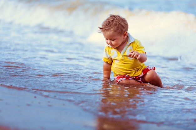 Piccolo bambino seduto vicino all'acqua del mare