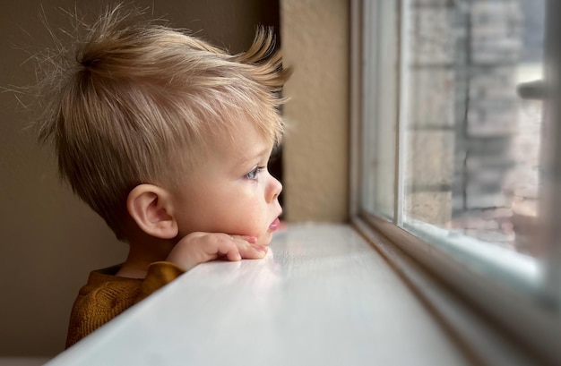 Piccolo bambino sveglio che guarda la finestra a casa, primo piano ritratto