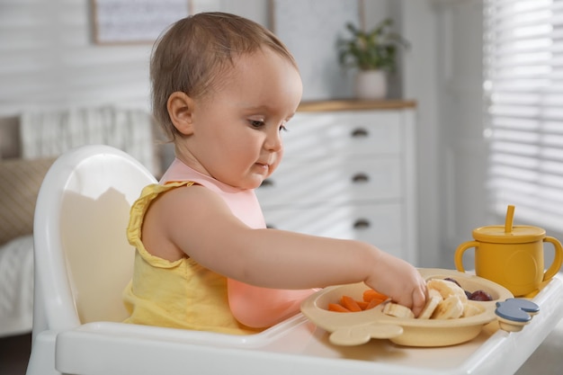 Piccolo bambino sveglio che indossa bavaglino mentre mangia a casa