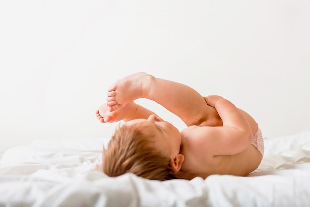 Piccolo bambino sveglio che si trova sul letto bianco e che sorride felicemente