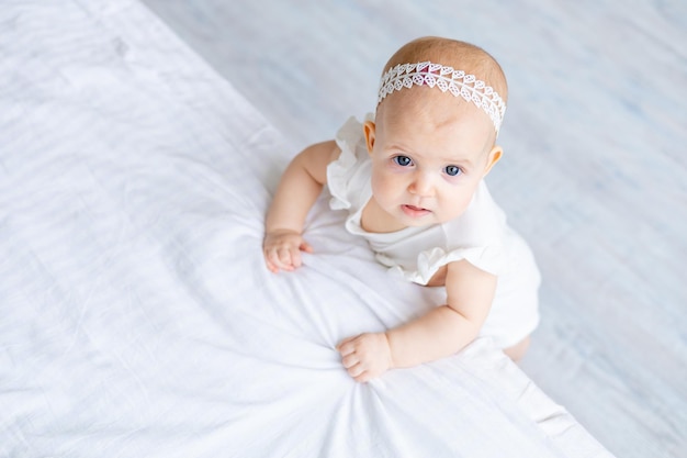 Piccolo bambino sveglio in una neonata del body di cotone bianco su un letto leggero a casa nel primo piano della scuola materna