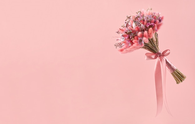 Piccolo bouquet di fiori secchi rosa a maglia con un nastro di raso rosa su rosa, copia spazio