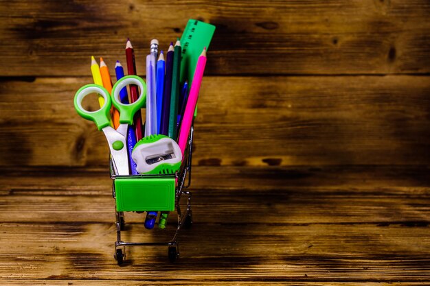 Piccolo carrello con diversi articoli di cancelleria per la scuola su fondo di legno rustico. Ritorno al concetto di scuola