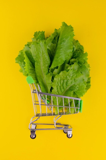 Piccolo carrello con foglie di lattuga verde su sfondo giallo brillante