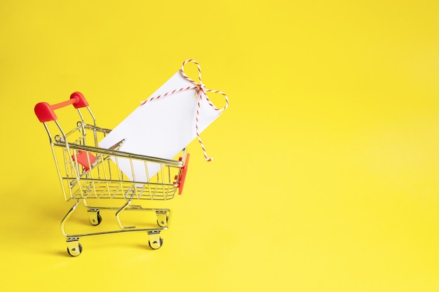 Piccolo carrello del supermercato con etichetta nera vuota su sfondo giallo.