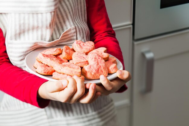 Piccolo chef che tiene i biscotti del cuore rosa. Biscotti a forma di cuore rosa fatti in casa per San Valentino