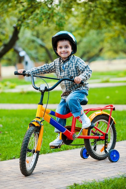 Piccolo ciclista. Ragazzino allegro che guarda la macchina fotografica e sorride mentre va in bicicletta