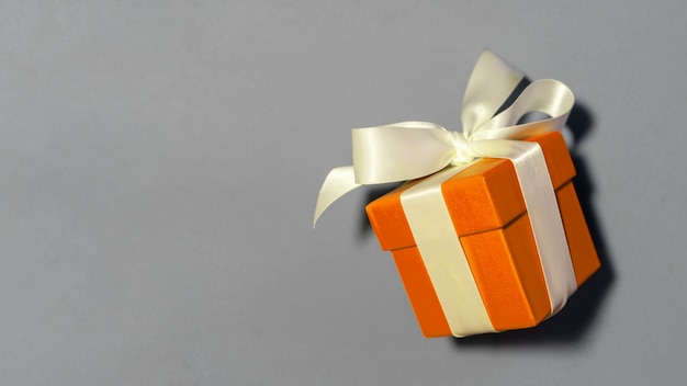 Piccolo contenitore di regalo arancione legato con un nastro dell'arco su una tabella grigia