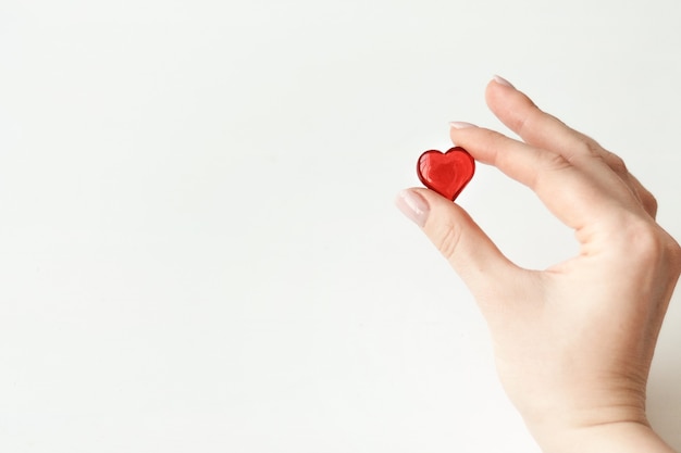 piccolo cuore rosso che tiene la mano con due dita su sfondo chiaro, il giorno di San Valentino