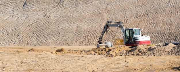 Piccolo escavatore bianco e rosso che muove terra nel mezzo di un grande cantiere da costruire