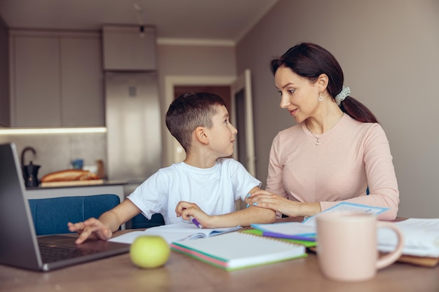 Piccolo figlio adolescente caucasico che guarda la madre mentre impara al computer portatile in una stanza accogliente