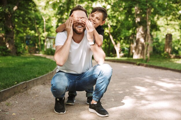 Piccolo figlio felice che copre gli occhi di suo padre allegro