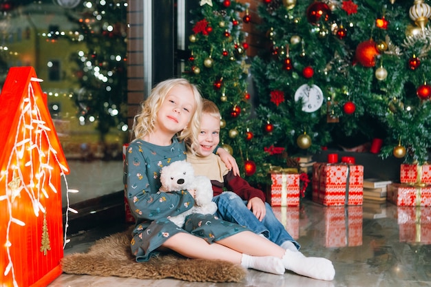 Piccolo fratello e sorella biondi svegli che posano all'albero di Natale