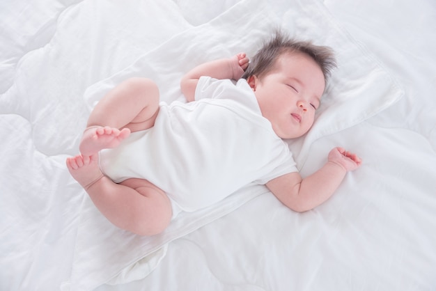 Piccolo infante asiatico che dorme sul letto bianco di mattina