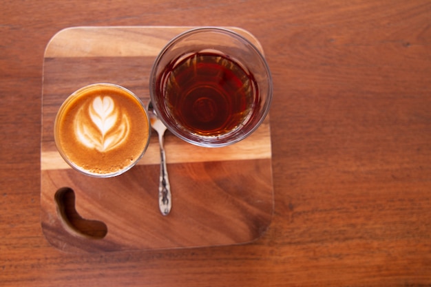 Piccolo Latte art in vetro piccolo con tè caldo sulla scrivania in legno.