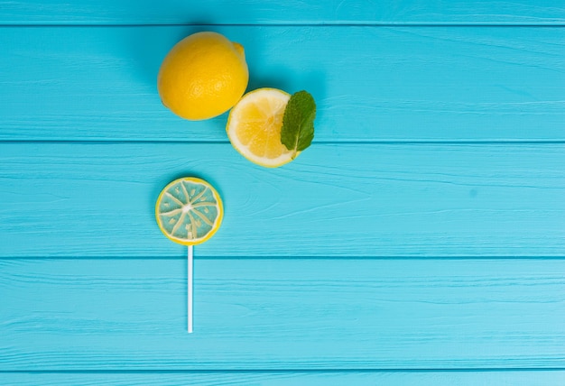 Piccolo lecca-lecca come limone su tavola turchese di legno vicino a un delizioso limone a fette e un rametto di menta