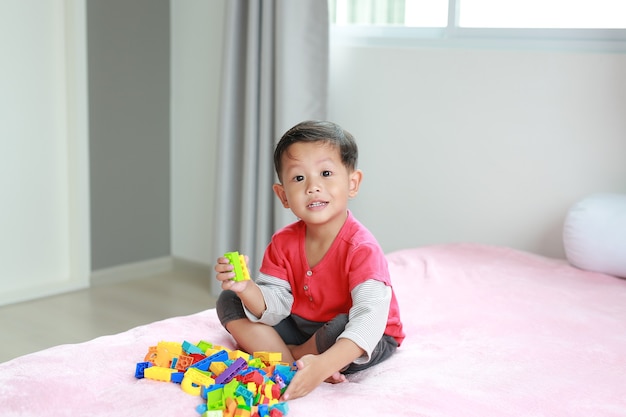 Piccolo neonato asiatico che gioca blocchi di plastica colorati e sdraiato sul letto.