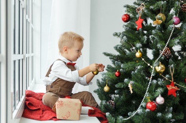 Piccolo neonato che decora i giocattoli dell'albero di Natale. Vacanze, regalo e concetto di Capodanno.