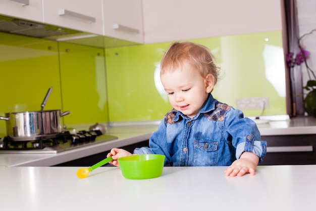 Piccolo neonato che mangia da solo usando il cucchiaio. Bambino che guarda sul piatto verde