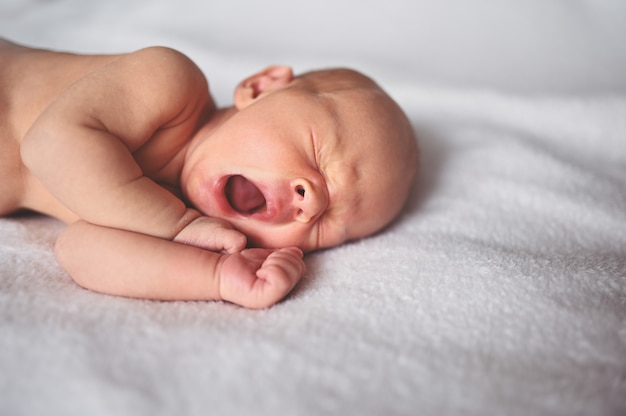 Piccolo neonato che sbadiglia divertente emotivo sveglio che dorme nella culla.