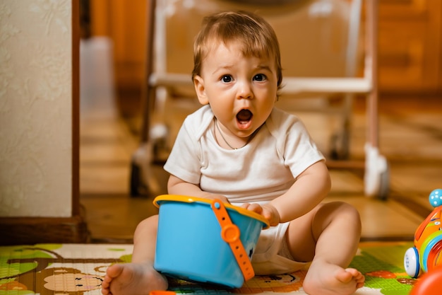 Piccolo neonato sveglio che gioca con i giocattoli educativi colorati sul tappeto da gioco all'interno della casa