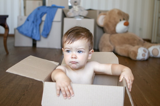 Piccolo neonato sveglio che si siede dentro la scatola di cartone che sogna della sua casa futura