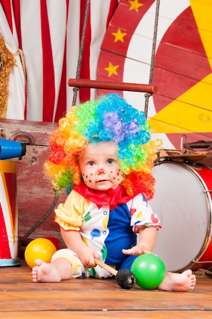 Piccolo pagliaccio del bambino con la parrucca multicolore del naso rosso dentro con le sfere.