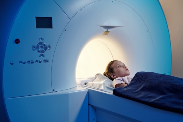 Piccolo paziente sotto un asciugamano blu sdraiato sul lungo tavolo della macchina per la risonanza magnetica