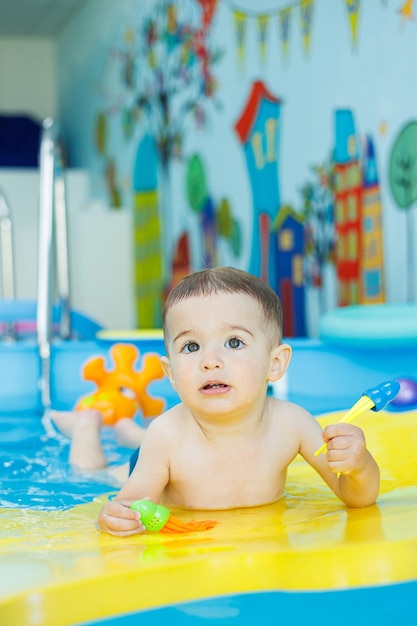 Piccolo ragazzo allegro di 2 anni sta imparando a nuotare in piscina Lezioni di nuoto per bambini Scuola di nuoto per bambini