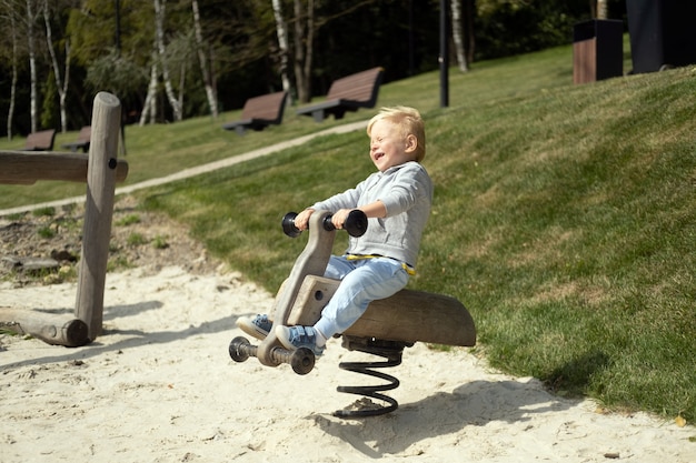 Piccolo ragazzo biondo caucasico che gioca nel parco giochi per bambini in una soleggiata giornata autunnale.