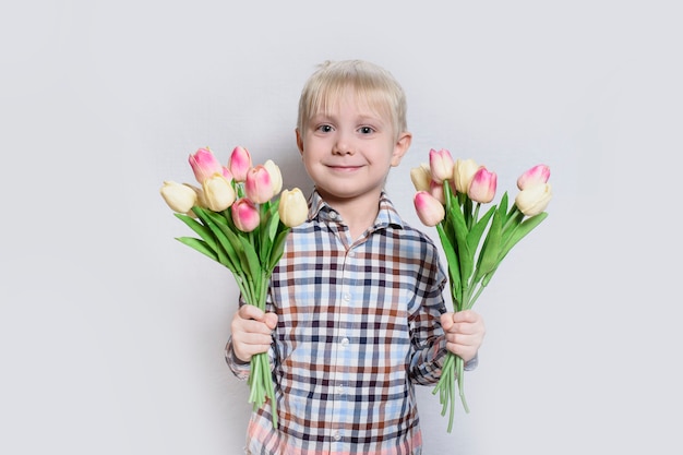 Piccolo ragazzo biondo sorridente che tiene un mazzo di tulipani.