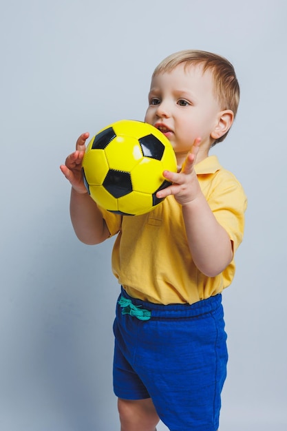 Piccolo ragazzo carino bambino ragazzo 34 anni tifoso di calcio in maglietta rossa tenendo in mano pallone da calcio isolato su sfondo giallo Bambini sport famiglia tempo libero stile di vita concetto Copia spazio pubblicitario
