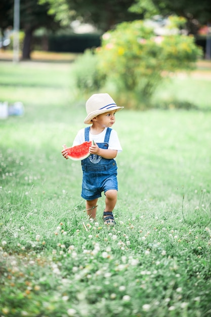 Piccolo ragazzo carino cammina nella foresta. Un ragazzino che mangia anguria. Estate.