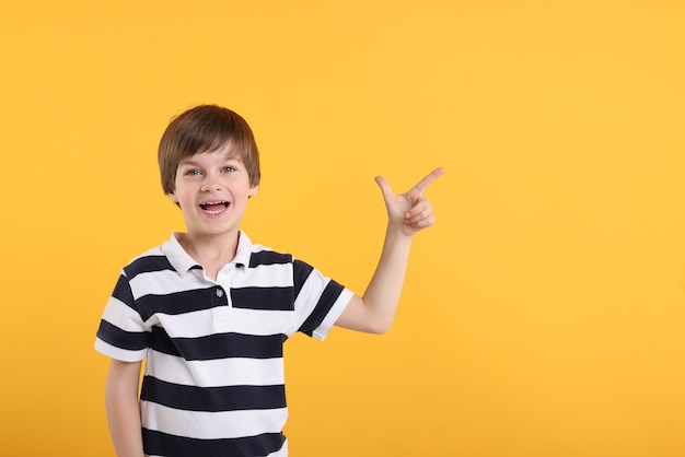 Piccolo ragazzo carino che indica qualcosa sullo sfondo arancione per il testo