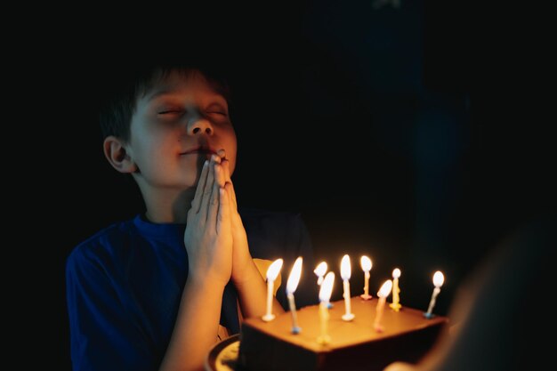 piccolo ragazzo caucasico carino che esprime un desiderio prima di soffiare una candela sulla torta per il suo 6 compleanno