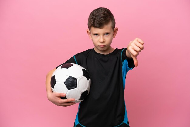 Piccolo ragazzo caucasico del giocatore di football isolato su sfondo rosa che mostra il pollice verso il basso con un'espressione negativa