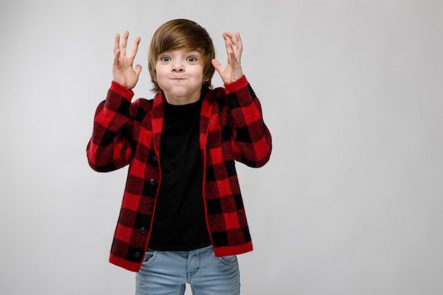 Piccolo ragazzo caucasico sicuro sveglio in camicia a quadretti che imbroglia mostrando il gesto grigio