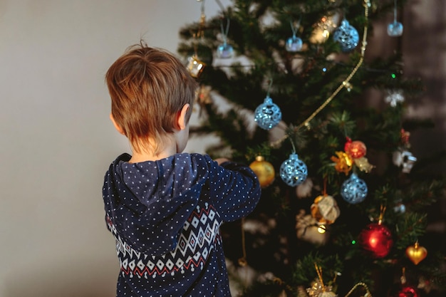 Piccolo ragazzo caucasico sveglio che decora l'albero di Natale con le decorazioni scintillanti