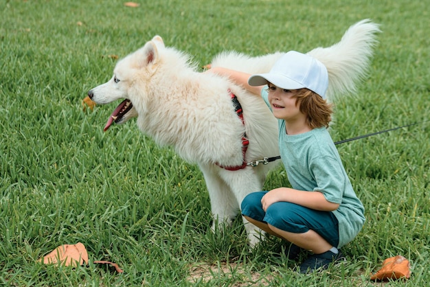 Piccolo ragazzo che abbraccia il soffice cane samoiedo bianco e ride nel parco o sullo sfondo dell'erba spirng