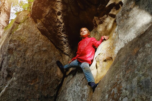 Piccolo ragazzo che si arrampica sulle rocce nella foresta. Bambino che si diverte e si avventura all'aperto. Attività pericolosa
