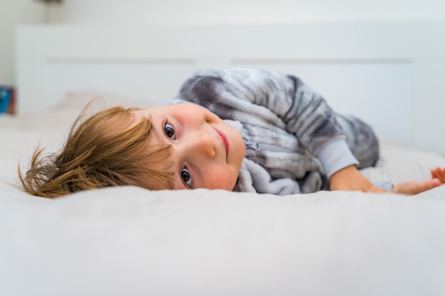 Piccolo ragazzo del bambino che si distende sul letto. Tempo libero a casa