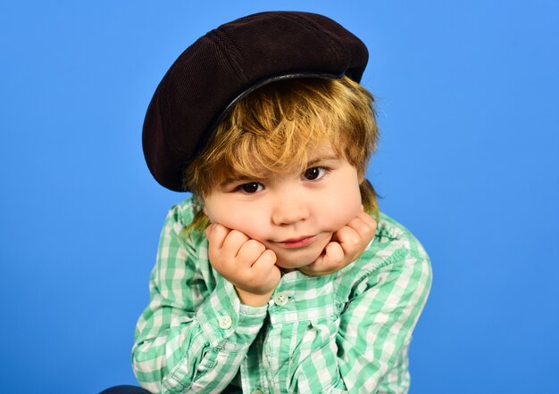 Piccolo ragazzo in camicia verde ragazzo tiene il viso sulle mani vicino ritratto alla moda bambino in cap