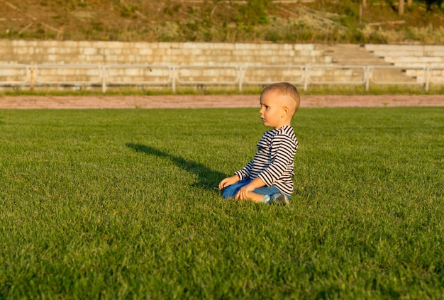 Piccolo ragazzo inginocchiato in erba verde alla luce del sole serale