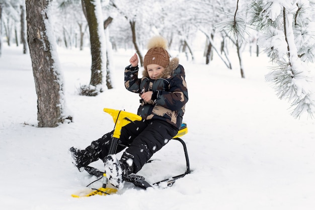 Piccolo ragazzo si siede su una slitta, gatto delle nevi in una foresta innevata.