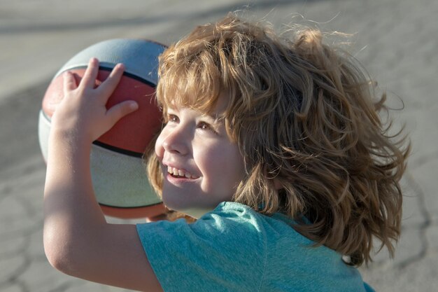 Piccolo ragazzo sportivo caucasico che gioca a basket tenendo la palla con la faccia felice