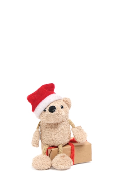 Piccolo simpatico orso morbido in cappello di Babbo Natale è seduto sul regalo box.Isolate su sfondo bianco.
