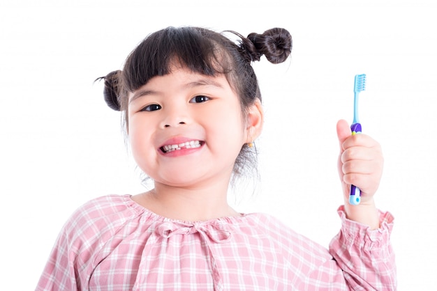 Piccolo spazzolino da denti e sorrisi asiatici della tenuta della ragazza sopra fondo bianco